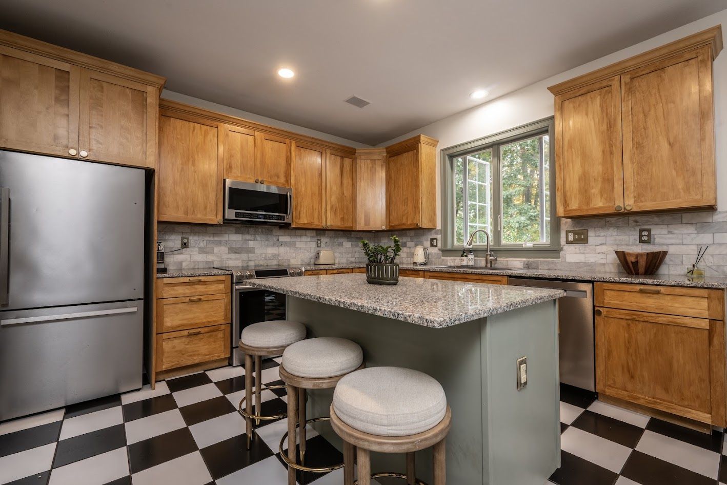 Kitchen with maple cabinets, granite island, stools and black and white checkerboard floor