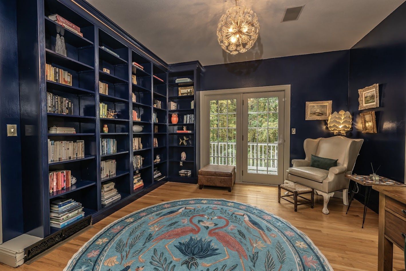 Home office with navy floor-to-ceiling bookshelves, a wingback chair and French doors to a balcony